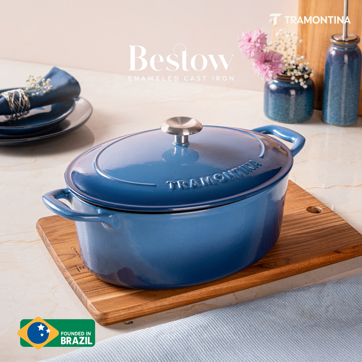 Tramontina India Bestow enameled cast iron oval Dutch oven in medium blue, 6.6L capacity, shown with lid on and cooking surface visible.