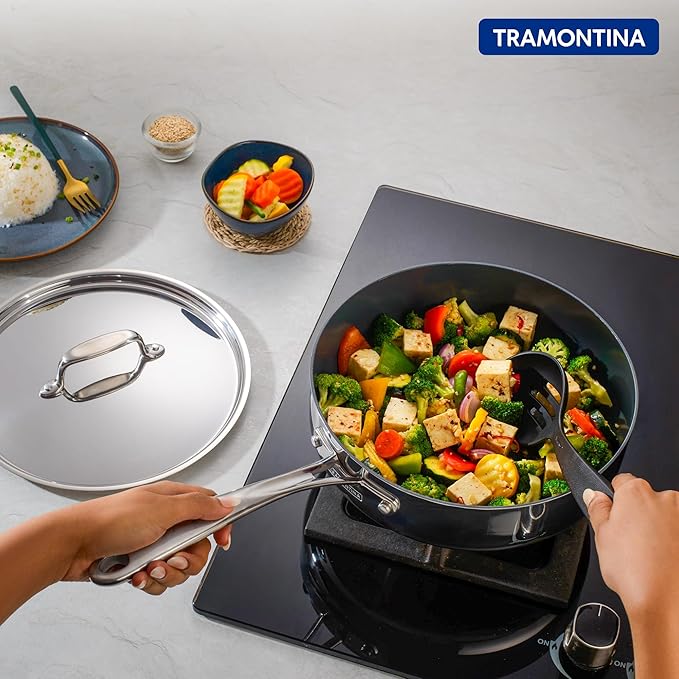 Tramontina India Fusao EX+ 24cm triply ceramic deep sauté pan with stainless steel lid, shown in a kitchen setting.