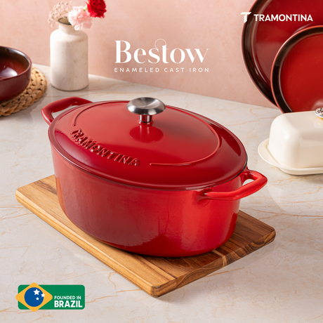 Tramontina India Bestow enameled cast iron oval Dutch oven in gradated red, 6.6L, showcasing its sturdy, glazed cookware with handles.